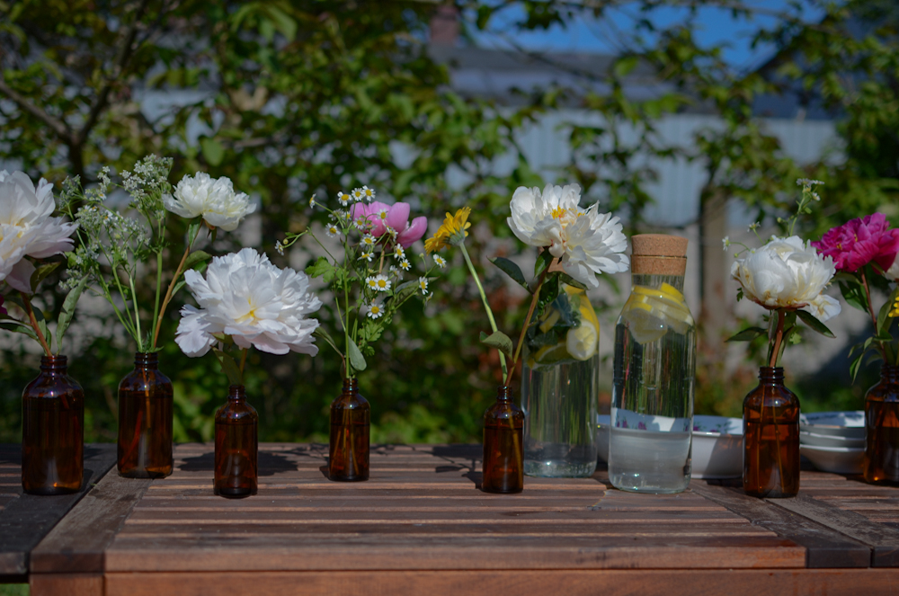 Niewielkie bukiety kwiatów w brązowych buteleczkach na drewnianym stole.
